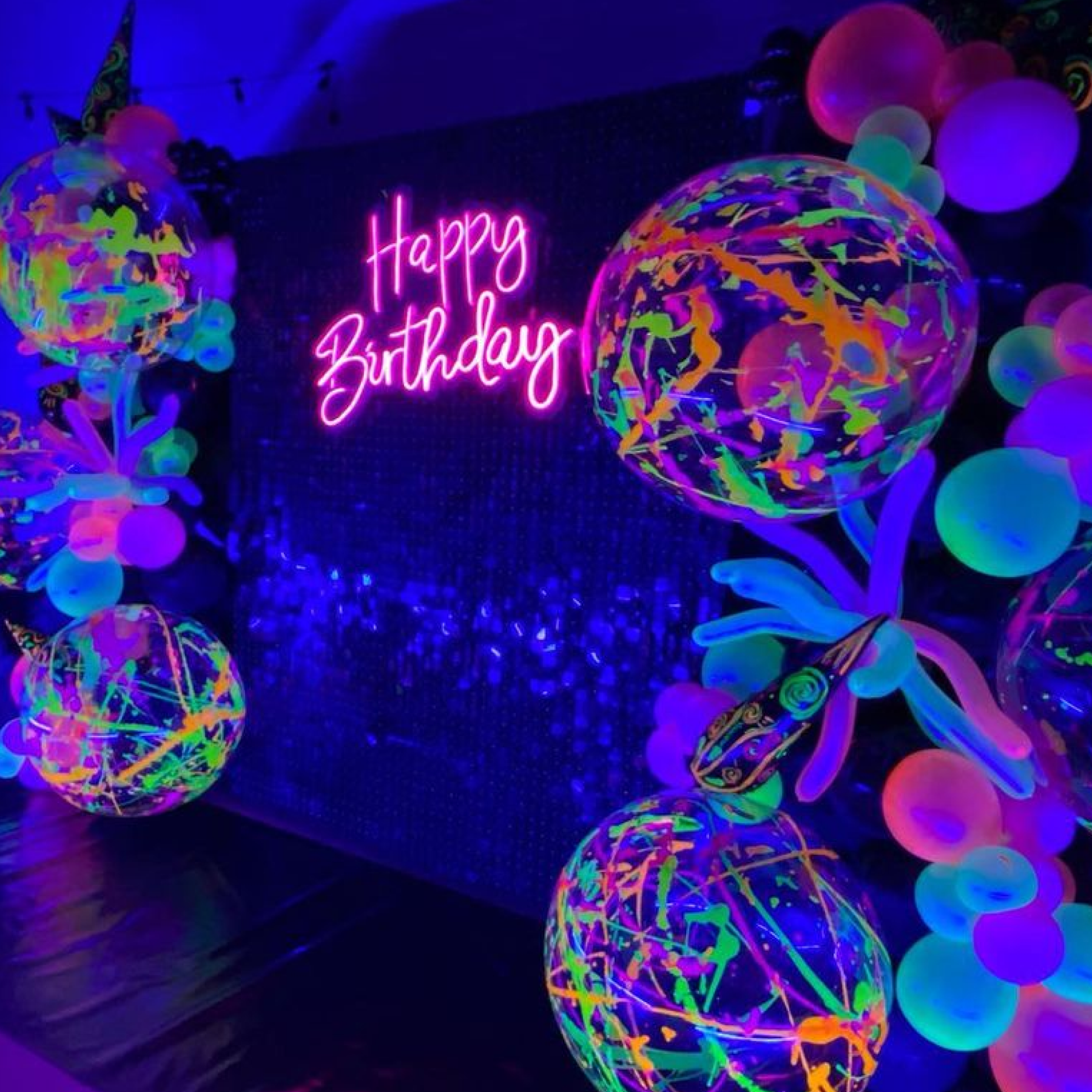 A neon sign that says "Happy Birthday" and colorful balloons.