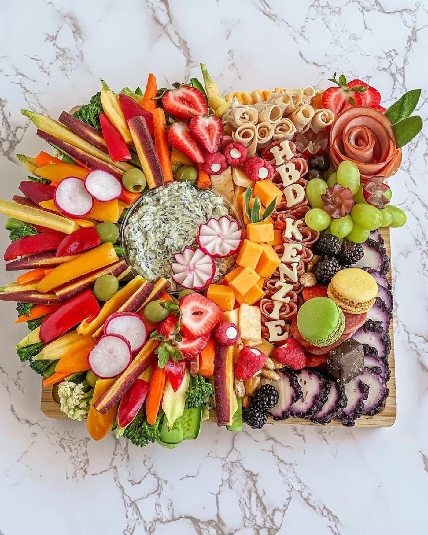 A charcuterie board with cheese cut out to say "HBD Kenzie."