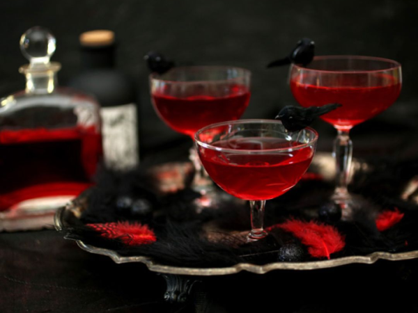 Three red cocktails with a decorative crow on the edge of each glass.