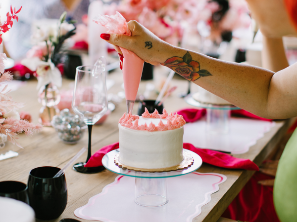 A woman decorating a cake with pink frosting.