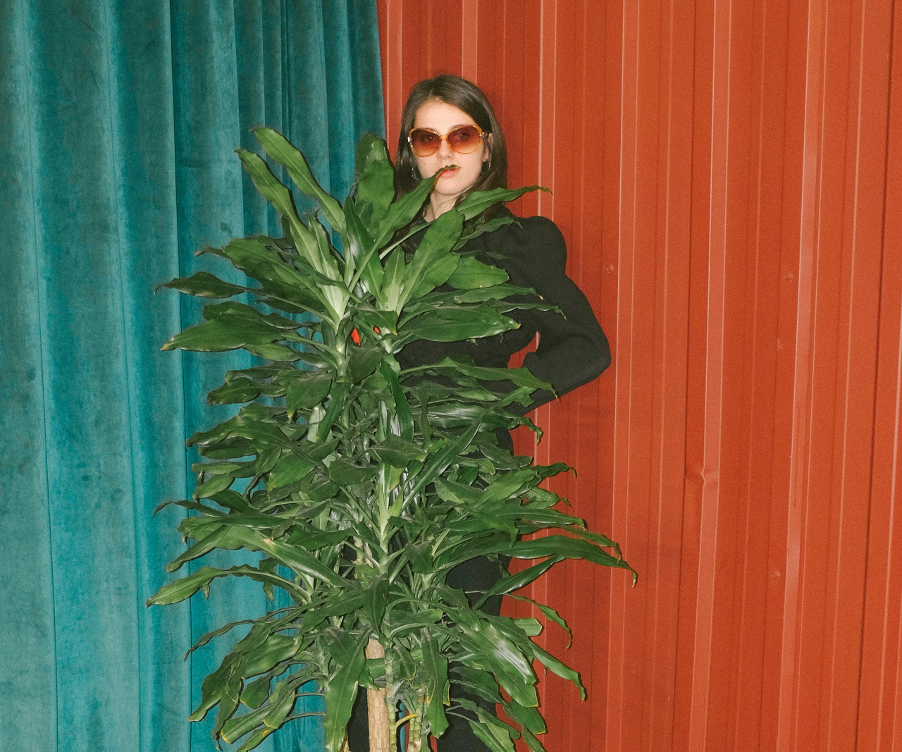 A girl in sunglasses standing being a house plant.