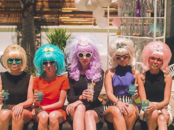 4 women sitting together wearing colorful beehive wigs and sunglasses.