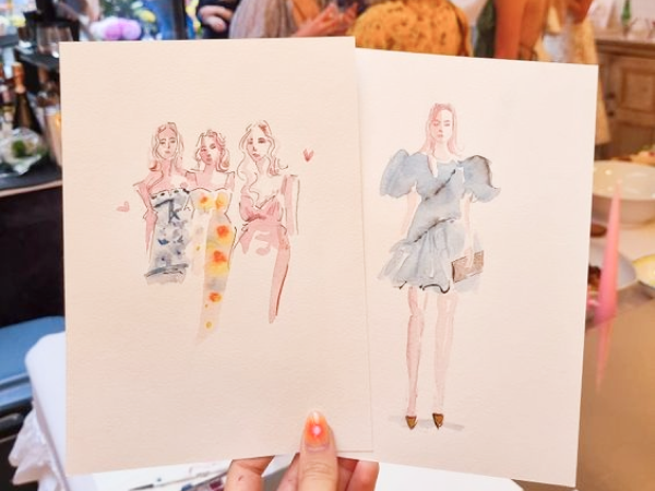 A hand holding fashion paintings at a party.